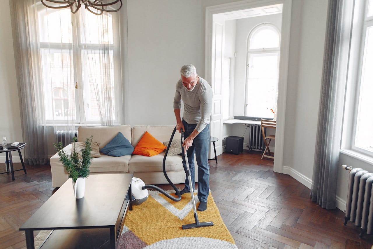 why-choose-us A senior man cleans the living room with a vacuum cleaner in a well-lit modern apartment.