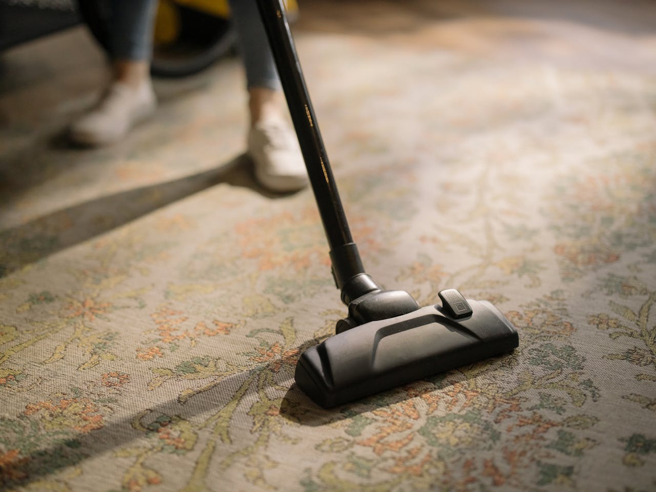 portfolio-03 Close-up of a vacuum cleaner on a patterned carpet in a sunlit room, capturing a moment of household cleaning.