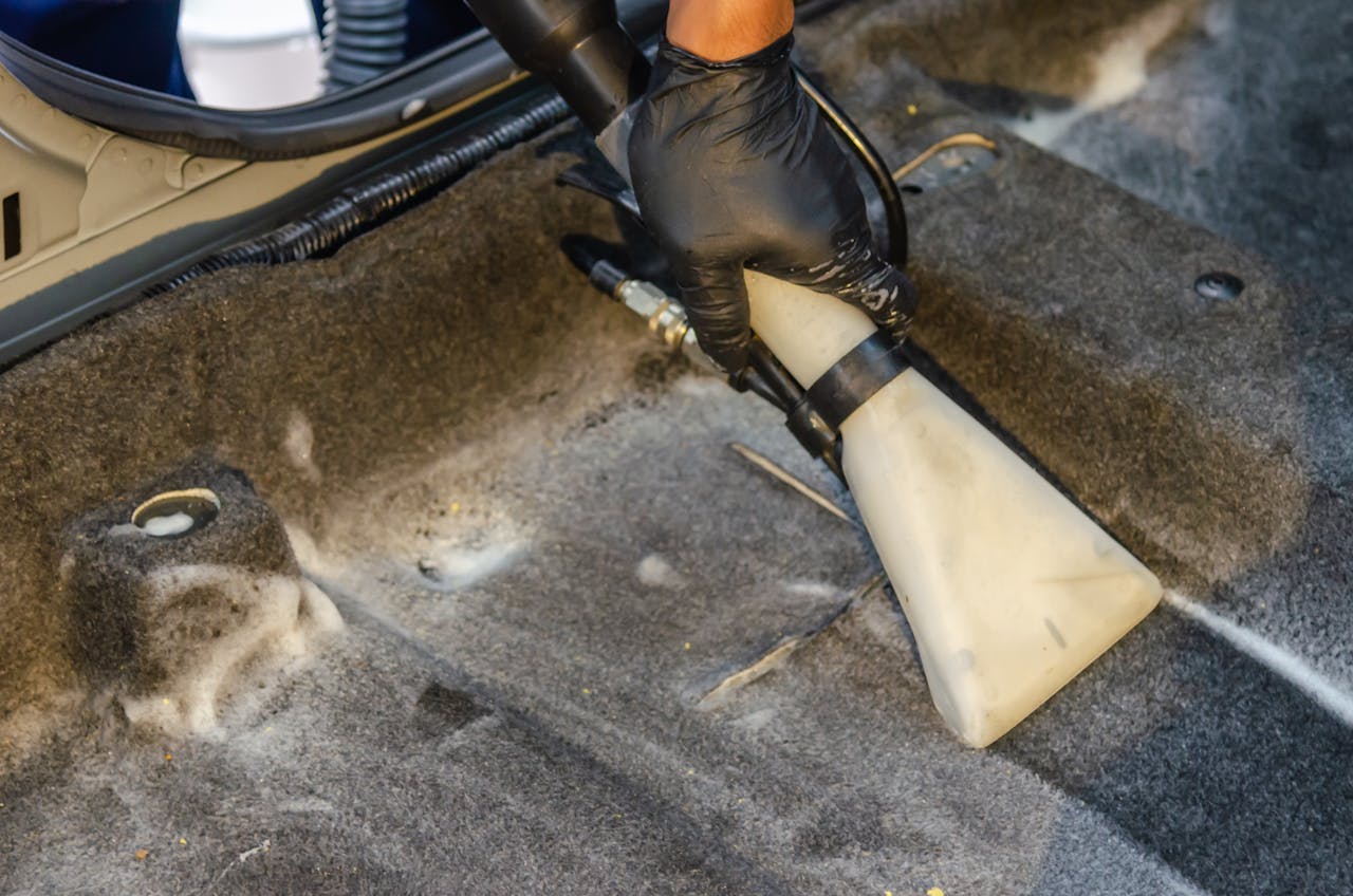stats-img A hand in a glove using a vacuum to clean a car interior carpet, removing dirt effectively.