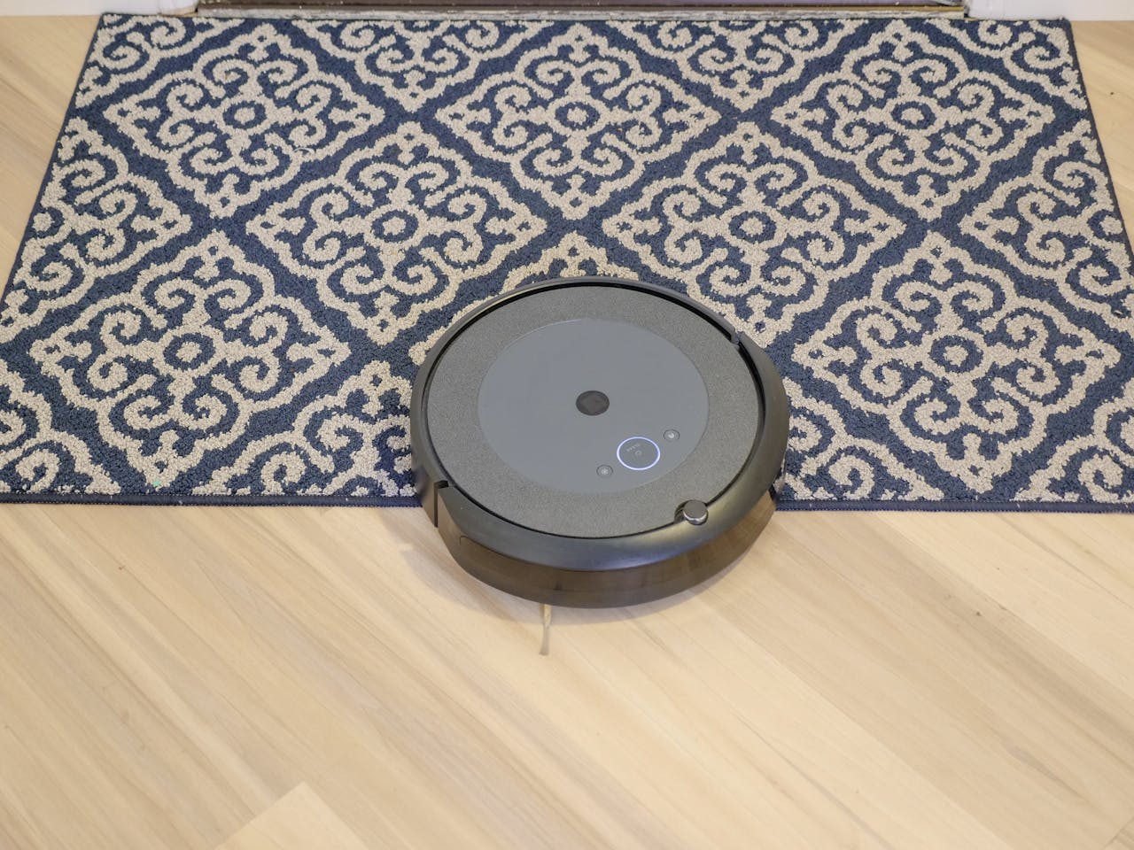 portfolio-05 A modern robotic vacuum cleaning a stylish patterned carpet on a wooden floor.