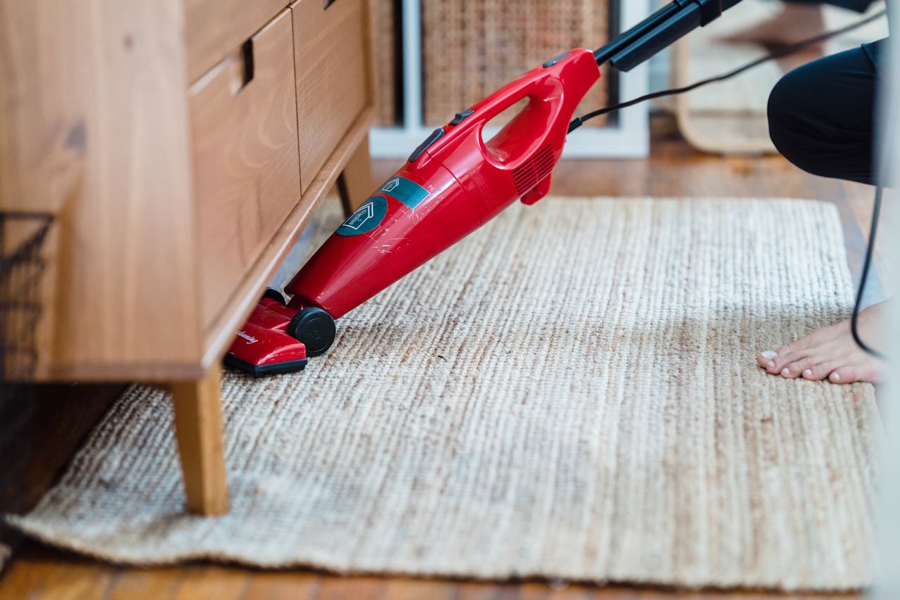 portfolio-06 Side view of a person using a red vacuum under furniture on a rug for effective cleaning.